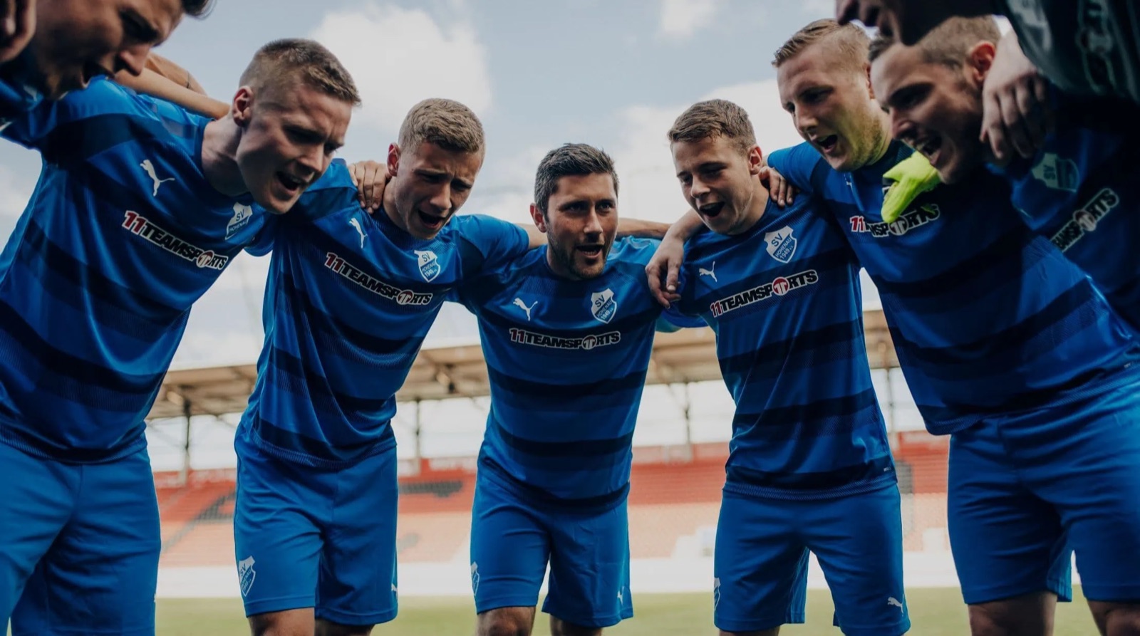 Mannschaft im Kreis vor dem Spiel, alle im gleichen Trikot mit Wappen und Sponsor